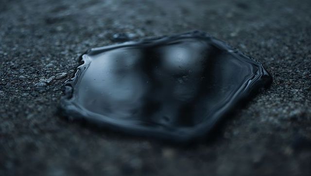 Dark glossy oil puddle reflecting faint highlights on coarse asphalt at dusk moody macro