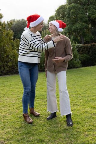 Mature friends wearing santa hats laughing and chatting on garden lawn
