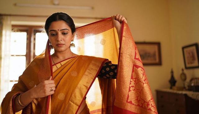 Draping indian woman adjusting mustard-gold silk saree pallu with jhumka earrings at home