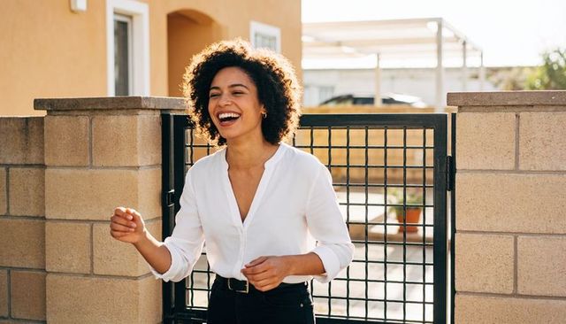Curly-haired woman laughing and enjoying golden hour by suburban gate