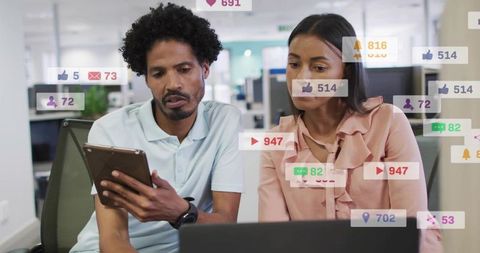 Two colleagues reviewing social media metrics on tablet and laptop in open office