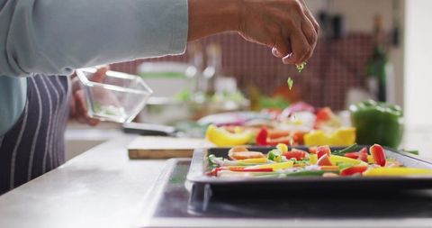 Elderly woman sprinkling fresh herbs on tray of colorful sliced peppers prepping dinner