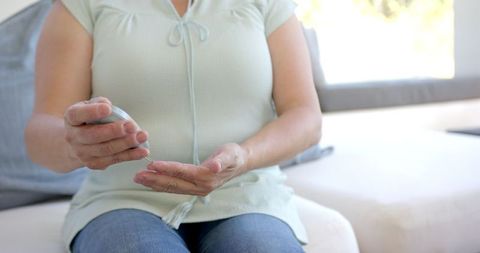 Asian Woman Applying Lotion for Skincare on Comfortable Couch