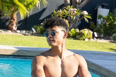 Young man relaxing at backyard pool wearing round sunglasses