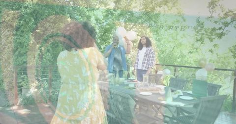 Woman taking phone picture of friends celebrating birthday on wooden deck with balloons