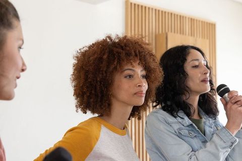 Multiracial women rehearsing vocals in bright minimalist studio with microphone