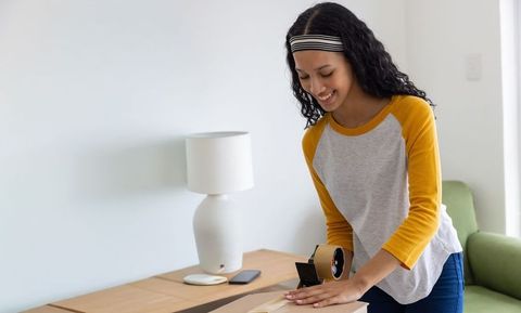 Teen girl sealing moving box in bright living room smiling while packing orders at home