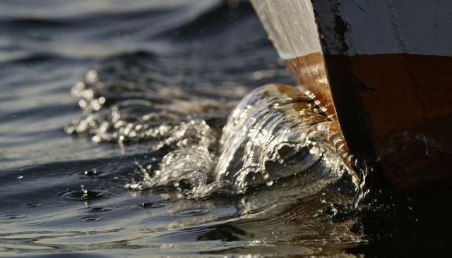 Boat bow cutting through harbor water at sunset creating splashing bow wave and ripples