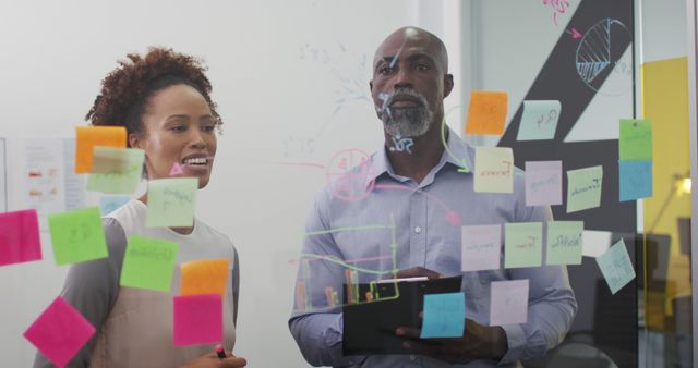 Diverse businessman and businesswoman brainstorming and smiling by transparent board with memo notes. working in a busy modern office.