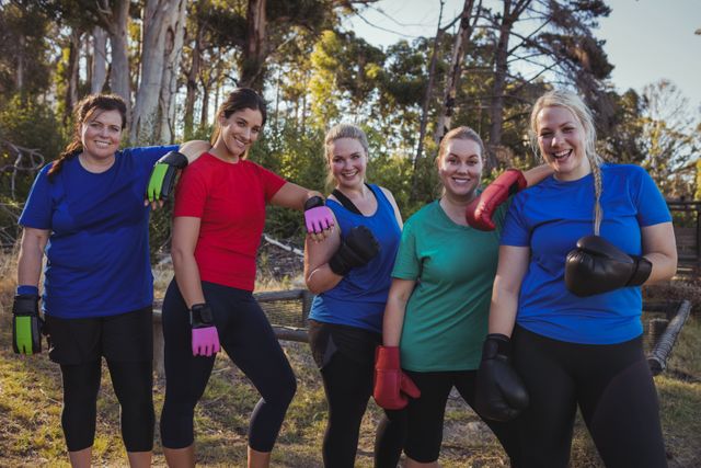 Group of fit women wearing colorful sportswear and boxing gloves, standing together and smiling after an outdoor boot camp session. Ideal for promoting fitness programs, women's health, teamwork, and outdoor activities.