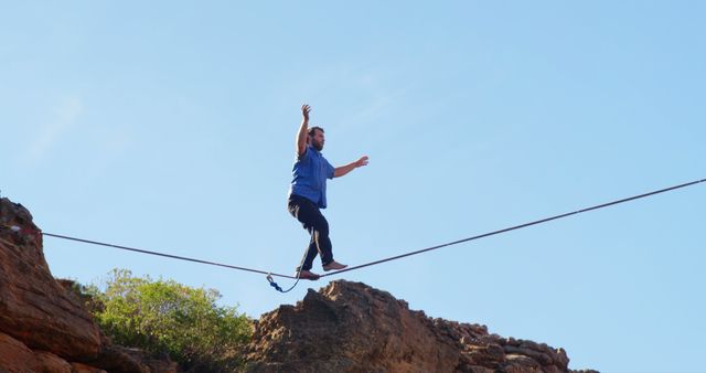 Man appearing focused while balancing on tightrope high above rocky cliff on sunny day. Great for illustrating concepts like courage, risk-taking, overcoming fear, and daring adventure. Useful for blogs, articles, and campaigns promoting outdoor activities, extreme sports, and inspirational themes.
