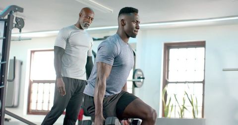 African american trainer coaching client performing weighted dumbbell lunge in bright gym