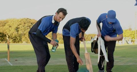 Diverse male cricket teammates resting on outfield with bat and equipment for practice