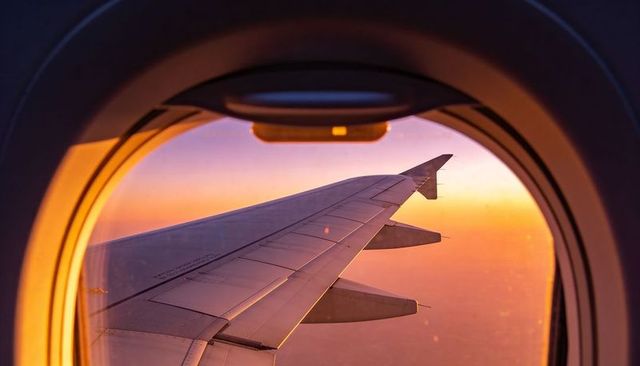 Sunrise wing view from passenger window showing winglet, rivets, gradient sky