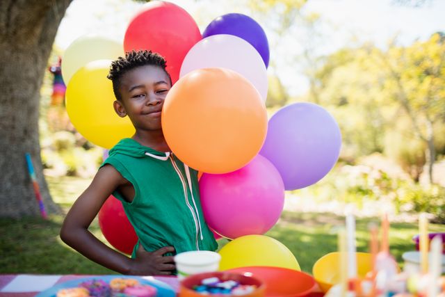 Boy smiling and posing with colorful balloons at an outdoor birthday party in a park. Ideal for use in advertisements, social media posts, and articles related to children's parties, celebrations, and family gatherings.