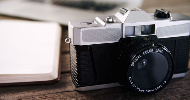 A vintage camera is positioned on a wooden surface next to an open notebook, with copy space. Its classic design evokes a sense of nostalgia and highlights the evolution of photography equipment over time.