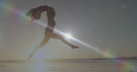 Leaping silhouette dancer on tidal flat with sunburst flare and starry dream overlay