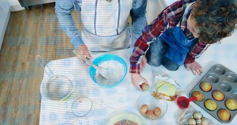 Parent and child baking together mixing muffin batter on bright kitchen countertop