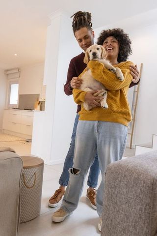 African american couple holding golden retriever puppy in modern home, smiling and hugging
