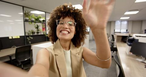 Smiling businesswoman waving in modern office workspace