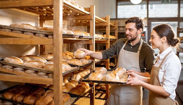 Artisanal Bakers Arranging Fresh Loaves on Wooden Racks in Rustic Bakery