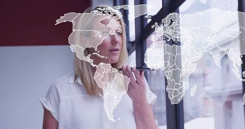 Female executive speaking into smartphone by office window with global map overlay