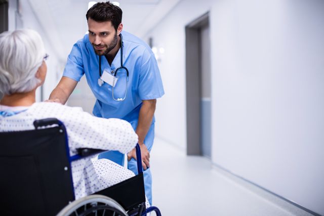 Male doctor interacting with senior patient on wheelchair in the corridor