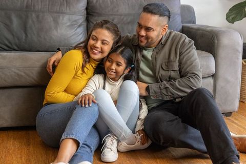 Smiling parents hugging daughter on living room floor cozy family moment at home