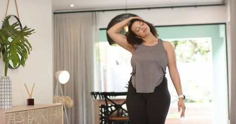 African american woman stretching neck in modern living room wearing smartwatch
