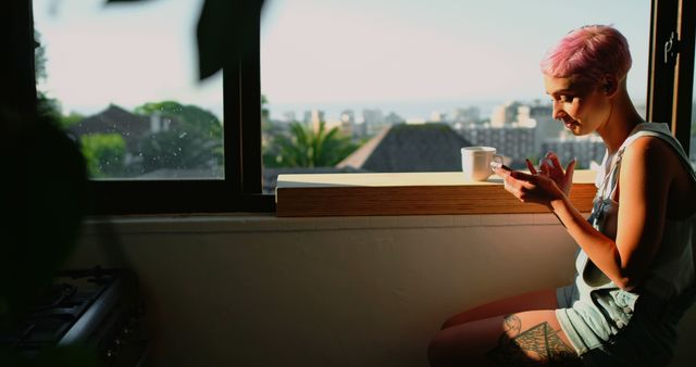 Young Woman with Pink Hair Enjoying Coffee and Using Smartphone near Window - Download Free Stock Images Pikwizard.com