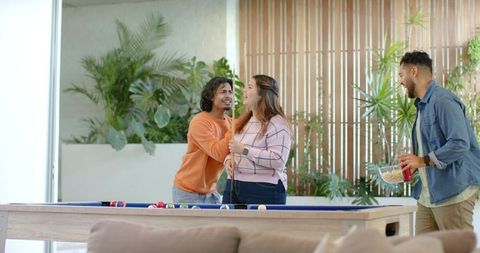 Friends Laughing Playing Pool in Bright Home Game Room with Blue Felt Table and Snacks