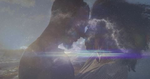 Silhouetted couple with cosmic clouds by moonlit ocean