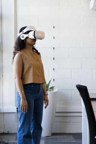 Woman wearing white VR headset and headphones standing in modern office near window