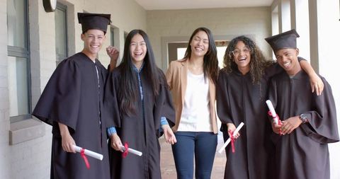 Diverse Graduates Celebrating with Mentor under Covered Corridor Holding Diplomas