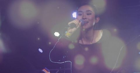 Singer in black top performing under spotlights with artistic bokeh