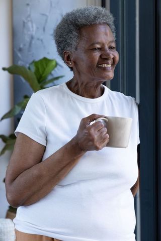 Senior african woman standing by doorframe holding mug, relaxed morning at home