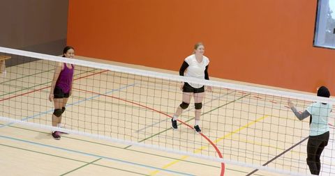 Diverse female teammates practicing volleyball in school gym wearing knee pads