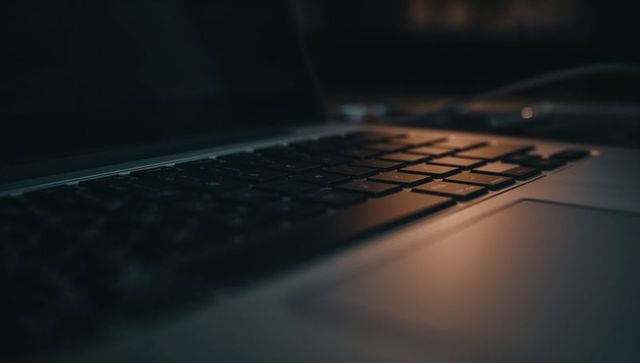 Glowing laptop keyboard and aluminum palm rest illuminating dim modern workspace