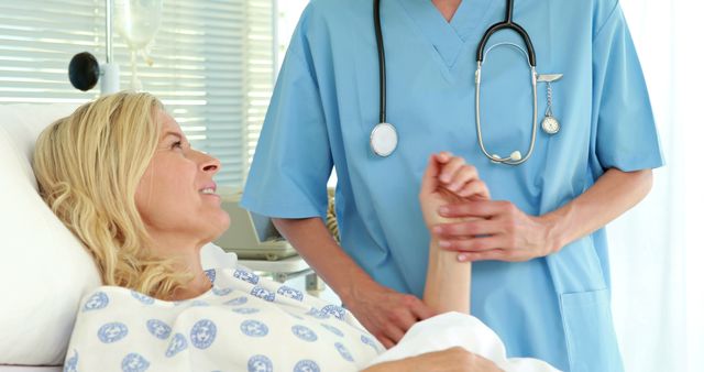 Doctor in blue scrubs checking pulse of female patient lying in hospital bed. Ideal for healthcare, patient care, doctor-patient interaction, medical services promotion, and hospital advertisements.