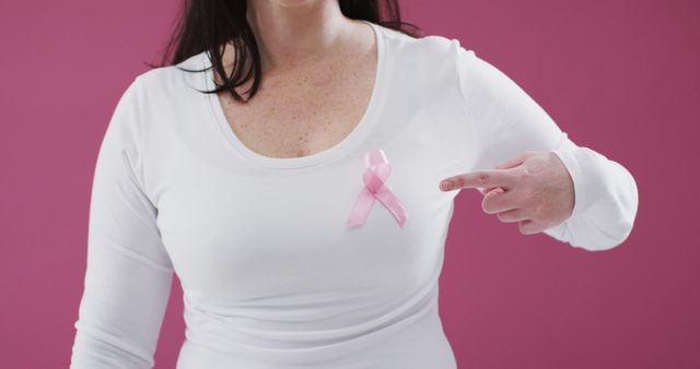 Woman Pointing to Pink Ribbon on White Shirt Against Pink Background - Download Free Stock Images Pikwizard.com