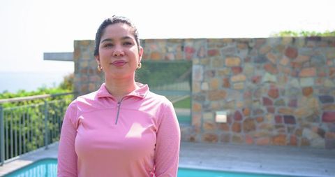 Woman standing on pool deck in pink pullover and hoop earrings, sunny patio lifestyle