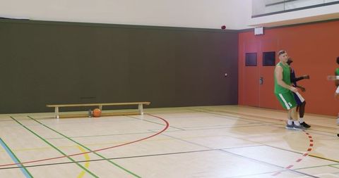 Diverse male basketball players shaking hands and jogging on indoor court after rebound