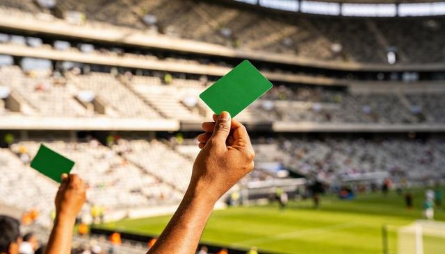 Fans raising green cards in stadium showing support and cheering during soccer match
