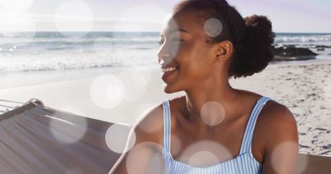 Sunlit beach hammock smiling young woman relaxing in striped swimwear with lens flare