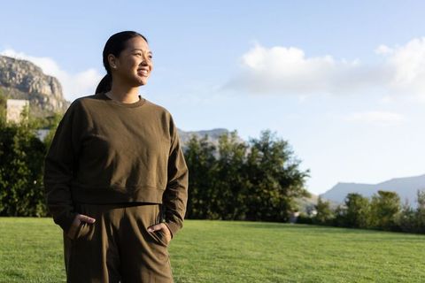 Smiling asian woman enjoying outdoor relaxation in olive athleisure on sunny lawn