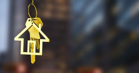 Golden House Keychain Hanging Against Blurred Cityscape Background
