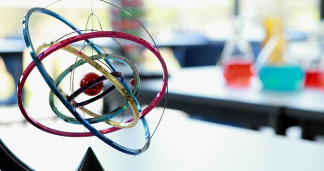 A model of an atom hangs in focus, symbolizing scientific education, with copy space. In the blurred background, beakers with colorful liquids suggest a chemistry laboratory setting.