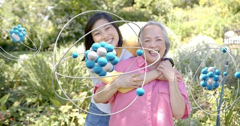 Smiling daughter hugging mother in sunlit garden with orbital metal sphere sculptures
