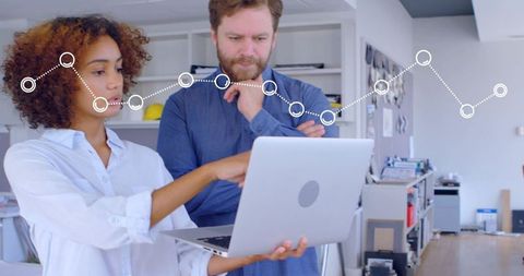 Collaborating colleagues analyzing data on laptop with overlay graph in modern office