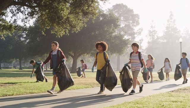 Children volunteering cleaning park walking with trash bags and gloves community cleanup